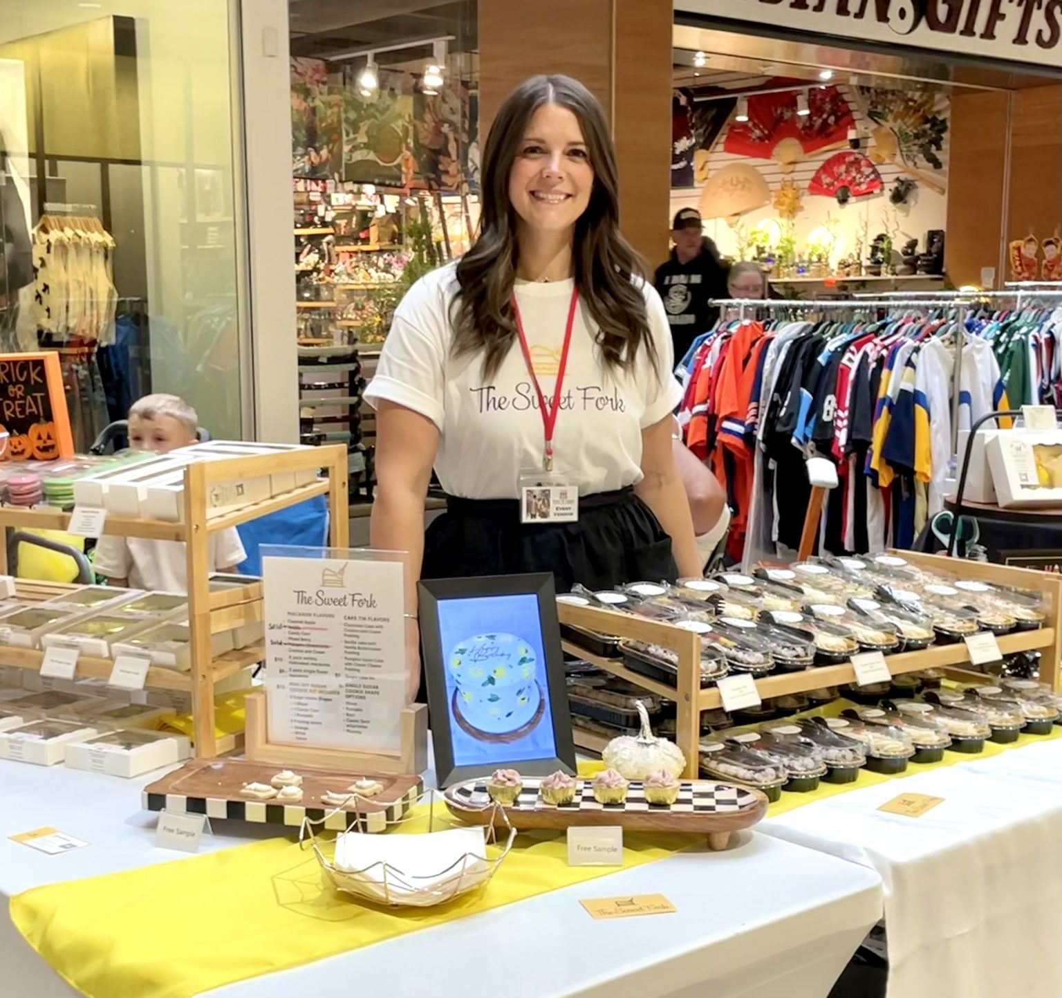 The Sweet Fork vendor booth display with packaged desserts, menu signage, samples, and bakery branding at an indoor event.